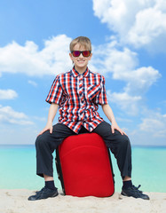 Fototapeta premium Happy boy with his luggage, tropical beach background
