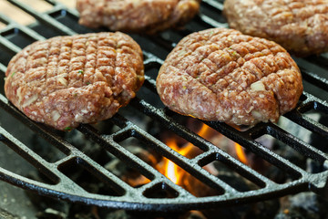 Raw burgers on barbecue grill with fire
