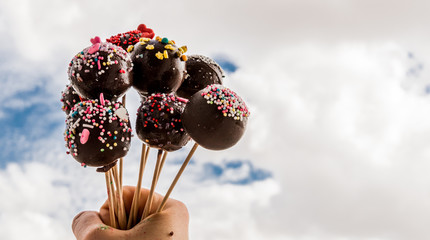 Cake pops in a hand in front of the cloudy sky