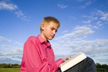 The boy reads the book outdoors
