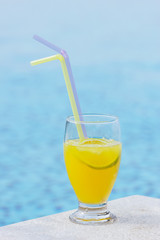 Glass of orange juice  against swimming pool.