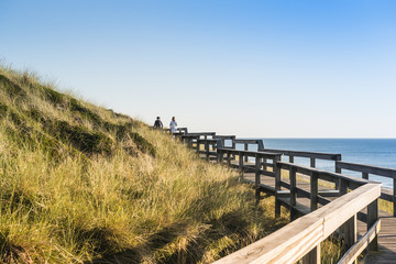 Fototapeta na wymiar People on wooden footpath on dune at beach in Germany.