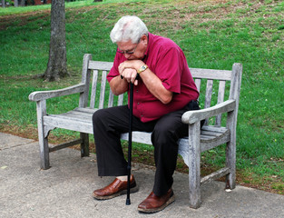 Fototapeta premium Elderly Man With Cane Sitting on a Park Bench
