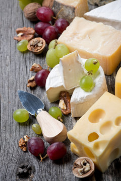 cheeses, grapes and walnuts on a wooden background, top view