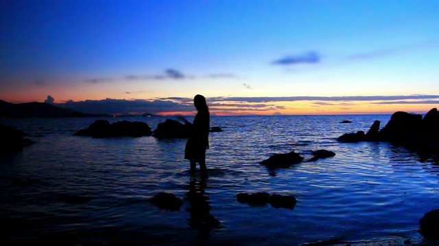 Silhouette of woman walking on a rocky beach during amazing