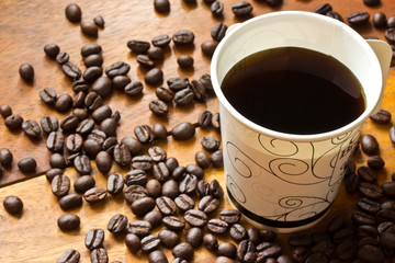 a paper cup of black coffee and coffee beans on wooden table