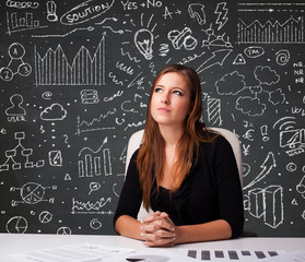 Fototapeta premium Businesswoman sitting at desk with business scheme and icons