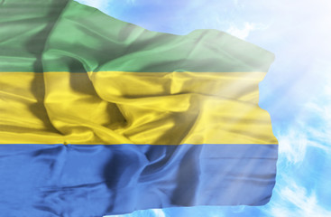 Gabon waving flag against blue sky with sunrays