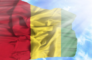 Guinea waving flag against blue sky with sunrays