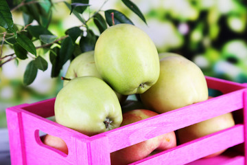 Juicy apples in box on wooden table on nature background