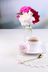Composition of beautiful peonies in vase, tea in cup and