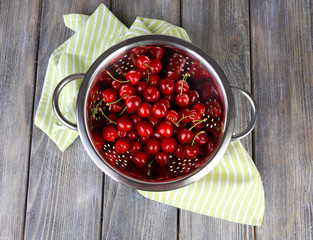 Sweet cherries in colander on color wooden background