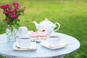 Coffee table with teacups and tasty cakes in garden