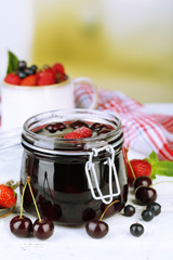 Tasty jam with berries in glass jar on wooden table