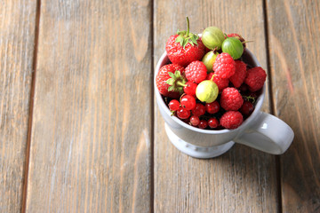 Forest berries in cup, on wooden table background