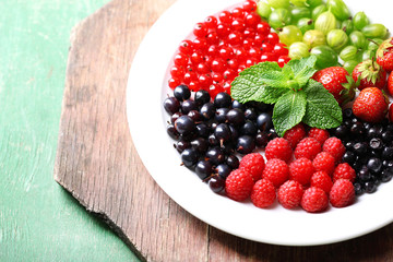 Forest berries on plate, on color wooden background