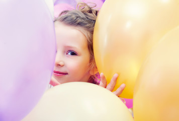 Fototapeta na wymiar Cute little girl peeking out from behind balloons