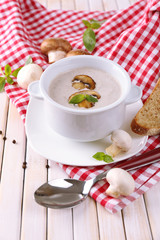 Mushroom soup in white pot, on napkin, on wooden background
