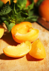Ripe apricots with green mint leaves on wooden background