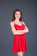 Beautiful young girl in red dress on grey background