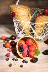 Different ripe berries in sugar cones, on wooden background