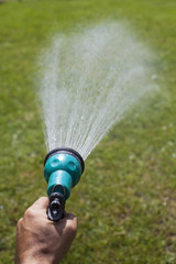 male hand holding a shower that sprayed water on the lawn
