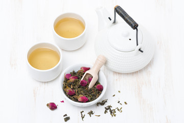 green tea with rosebuds, cups, teapot on white table, top view