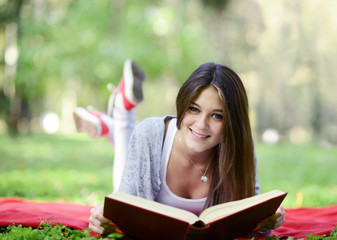 Beautiful smiling woman reading book in park