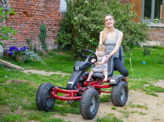 Little cute boy driving pedal car with young mother