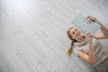 Smiling woman laying on wooden floor with tablet