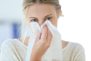 Young woman with cold blowing her runny nose - obrazy, fototapety, plakaty