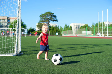 Obraz premium Little girl football fan on the green grass field with ball