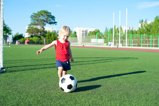 Little girl football fan on the green grass field with ball