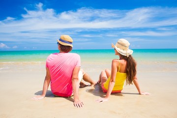 happy young couple in straw hats sitting at beach