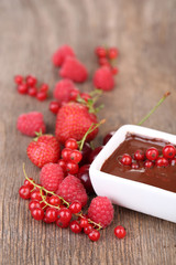 Ripe sweet berries and liquid chocolate on wooden table