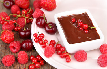 Ripe sweet berries and liquid chocolate on wooden table