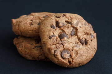 Three chocolate chip cookies on dark grey fabric.
