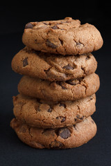 Stack of chocolate chip cookies on dark grey fabric.