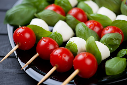 Red tomatoes, mozzarella and green basil on skewers, close-up