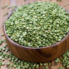 Wooden bowl with split dried green peas, close-up, studio shot