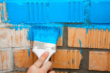 Paint brush with blue color on brick wall