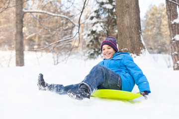 Fototapeta na wymiar young boy sledding on snow in park.