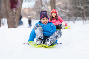 boy and girl sliding on sledges in park.