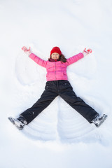 young girl laying on snow and making angel.