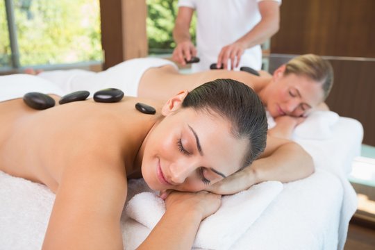 Calm friends lying on massage tables with hot stones on their ba