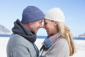 Attractive couple smiling at each other on the beach in warm clo