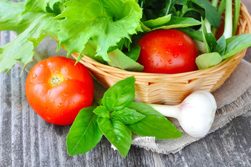 Fresh vegetables and greenery are in a basket on a old wooden ba