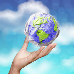 hand showing crumpled world paper symbol as concept on blue sky