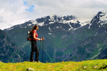 Young woman with backpack and trekking poles in mountains