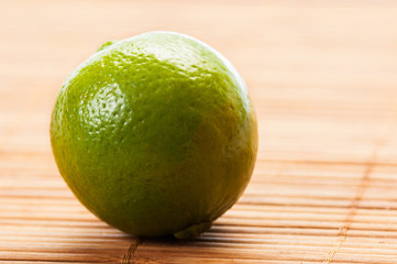 Closeup of a green lime on bamboo table.